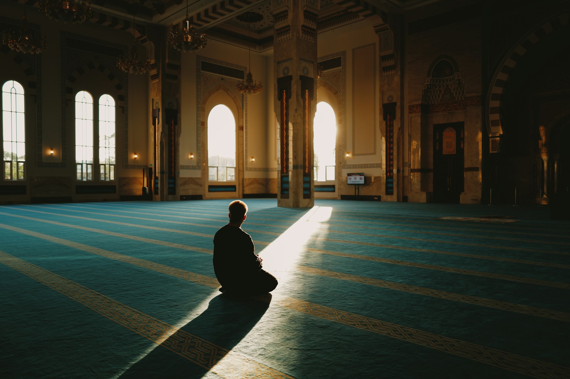Man sitting in a sunlit mosque prayer hall.